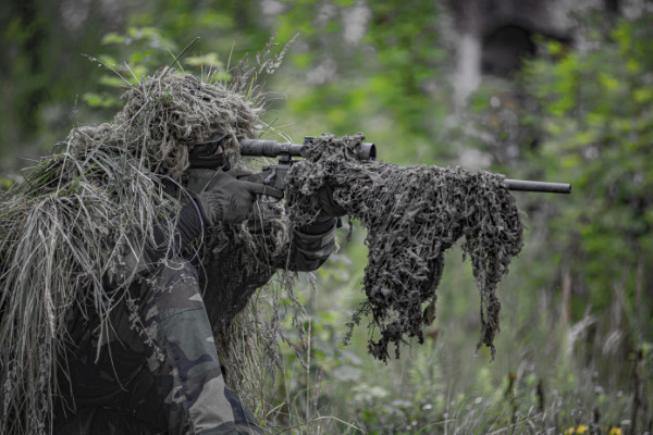 Sniper wearing a ghillie in selective focus photography military zoom background